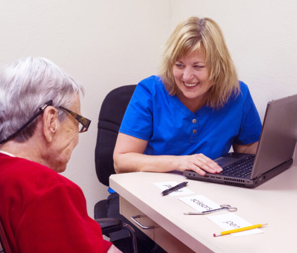 Blond Caucasian speech language pathologist laughs with a senior aged female aphasic patient during speech therapy session targeting visual comprehension skills. Patient realized she incorrectly matched objects to a field of three single written words.